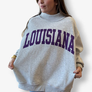 Person wearing a gray sweatshirt with 'LOUISIANA' printed in purple on a plain background