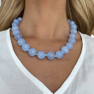 Light blue chunky beaded necklace with oversized glossy round beads styled on model front view against white top for statement jewelry styling.