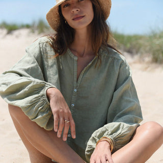     Sage green oversized linen top with balloon sleeves seated beach lifestyle view