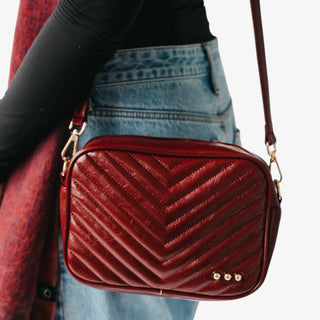 Burgundy quilted handbag with gold accents worn by a person