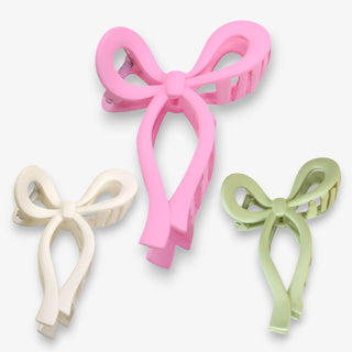 Three bow-shaped hair clips in pink, white, and green on a white background