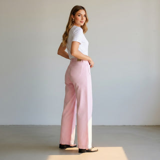 Woman wearing a white t-shirt and pink pants standing against a plain background