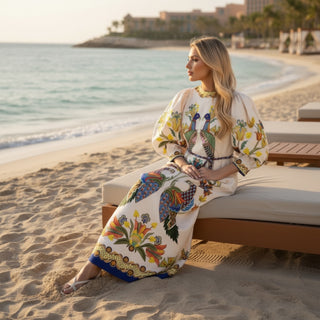 Peacock maxi dress with colorful bird print and puff sleeves on beach resort lounge chair