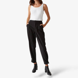 Woman wearing Michael Stars Maxine Twill pant in black with a white tank and black boots on a white background