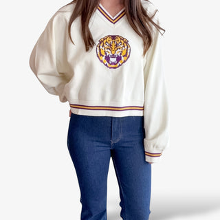 Person wearing a cream sweater with a tiger logo and blue jeans on a white background