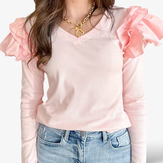 Women wearing a blush ribbed top with voluminous ruffled long sleeves and light wash denim jeans