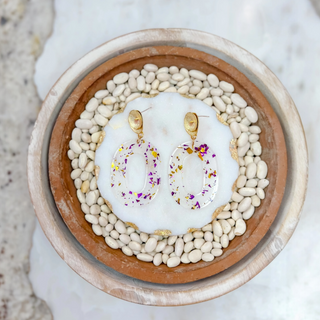 Clear oval earrings with gold and purple foil flakes and gold shell studs on white resin base.