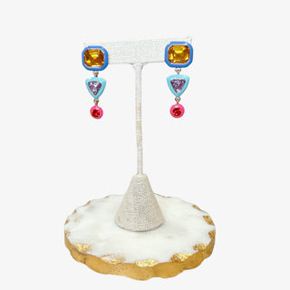 Colorful geometric drop earrings with yellow, lavender, and pink stones in bold resin shapes on display stand.