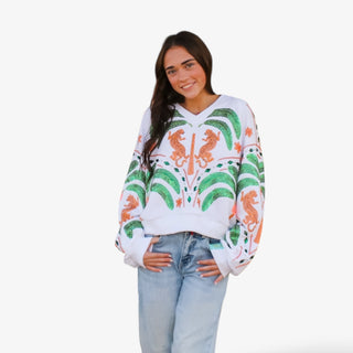 Woman wearing white Queen of Sparkles V neck sweatshirt with green palm trees and orange jaguar graphic details