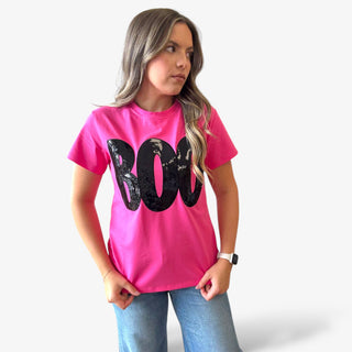 Person wearing a bright pink t-shirt with black sequin BOO letters on a plain background