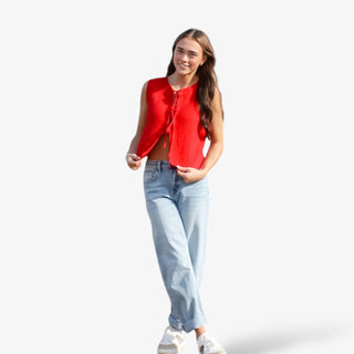 Woman wearing a red sleeveless top and light blue jeans on a white background