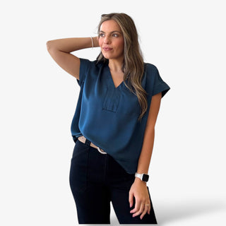 Woman wearing a blue v-neck top and black pants on a white background