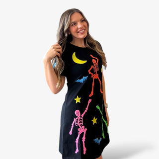 Woman wearing a black dress with colorful skeleton and moon designs on a white background