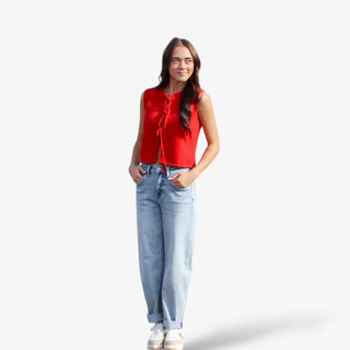Woman wearing a red sleeveless tie front top and light blue jeans on a white background