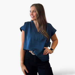 Woman wearing a blue satin v-neck top with black pants on a white background