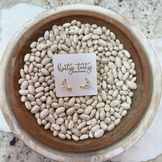 Small gold starburst stud earrings displayed on a Hoity Toity Boutique card, styled in a wooden bowl filled with white beans.