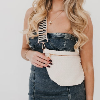 A cream woven sling bag with a wide black and white striped adjustable strap.