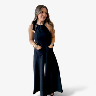Model wearing a black wideleg jumpsuit with tie detail and front pockets
