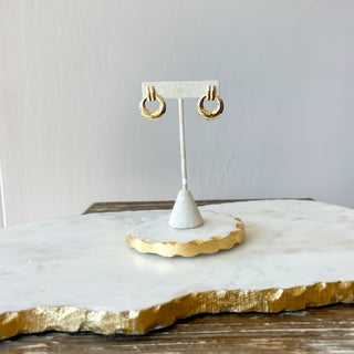 Gold hoop earrings on a white stand with a gold-edged white surface
