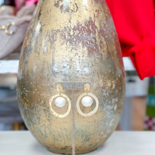 Gold earrings with cotton pearls on a metallic stand against a textured gold background