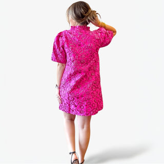 Person wearing a bright pink dress with a floral pattern on a white background