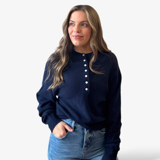 Woman wearing a navy blue sweater with white buttons and jeans on a white background