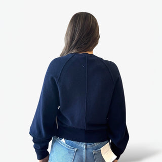 Person wearing a navy blue sweater and light blue jeans on a white background