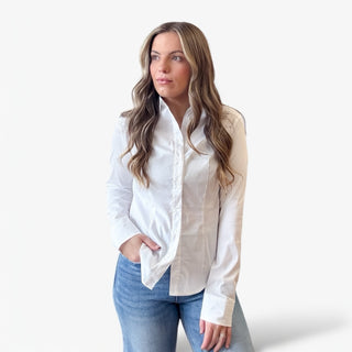 Woman wearing a white button-up shirt and blue jeans against a plain background