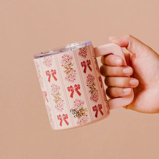 Hand holding a mug with floral and bow design on a beige background