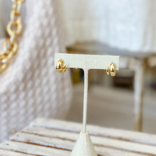 Gold double hoop earrings on a white earring stand with a blurred background