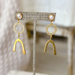 Gold pearl link wishbone drop earrings displayed on neutral jewelry stand