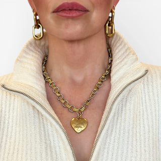 Close-up of a person wearing gold and silver chain necklace with a heart pendant and hoop earrings.