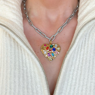 Person wearing silver necklace with  heart and multicolor gemstones and a cream sweater.