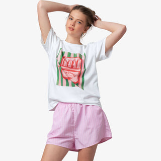 Woman wearing a white t-shirt with a graphic design and pink shorts on a white background