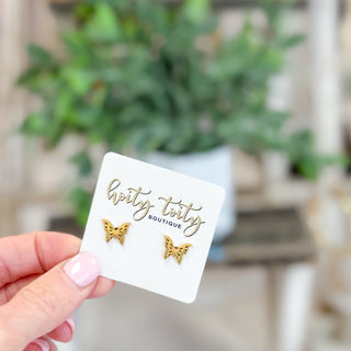 Gold butterfly earrings on a card held by a hand with a blurred green plant background