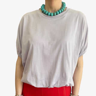 Person wearing a lilac top and red pants with a turquoise necklace on a white background