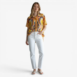 Aruba scarf print top in vibrant orange and blue tropical pattern styled with white straight leg jeans and white sandals on a female model against a clean white background
