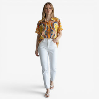 Aruba scarf print top in vibrant orange and blue tropical pattern styled with white straight leg jeans and white sandals on a female model against a clean white background