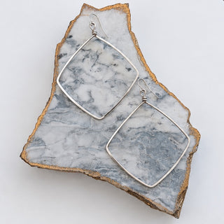 Kitzi Kaylee silver drop earrings with open diamond-shaped frames displayed on a marble stone, front product view.