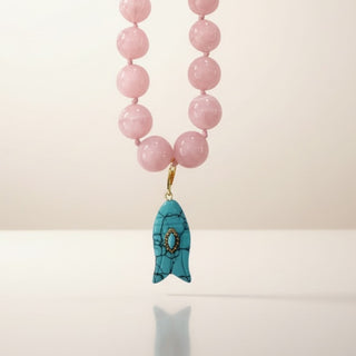 Close up of pink bead necklace with turquoise fish charm pendant and gold accent detail