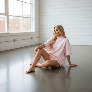 Woman in a pink short sleeve lounge short set sitting on a concrete floor in a bright room.