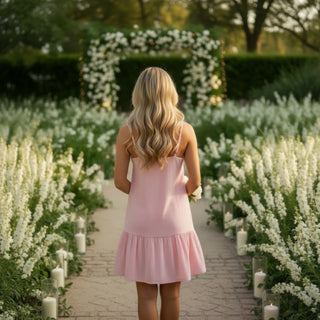 Pink sleeveless mini dress with tiered ruffle hem and spaghetti straps back view in garden setting