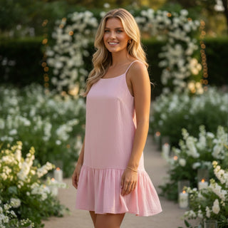 Pink ruffle mini dress with spaghetti straps and tiered hem styled as a wedding guest dress front view