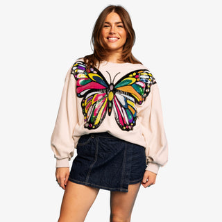 Woman wearing an oversized beige sweatshirt with a bold, colorful sequin butterfly design on the front.