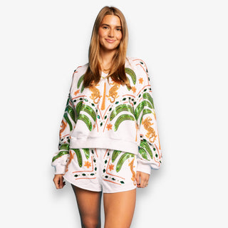 Woman wearing white Queen of Sparkles sweatshirt with green palm trees and orange jaguar graphic details