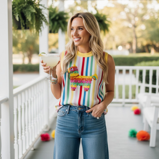 Woman in colorful striped sleeveless top and jeans holding a drink on a porch.