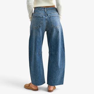 Raw hem barrel jeans in medium wash denim showing back pockets and curved leg seams, styled with tan suede mules, rear view