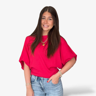 Woman wearing a red top with dolman sleeves and blue jeans on a white background