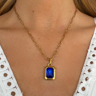 Sapphire emerald cut pendant necklace with deep blue gemstone in gold bezel setting on paperclip chain, worn layered on model, front