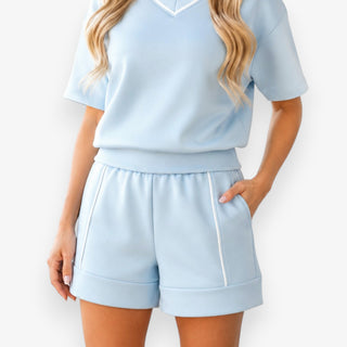 Powder blue scuba A-line shorts with white piping, front pockets and cuffed hem styled with matching V-neck top, close up view